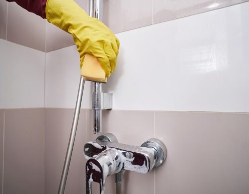 Housecleaner in rubber glove washing plumbing fixture
