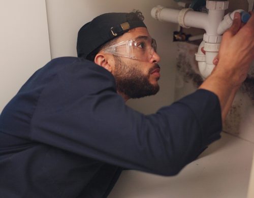 Plumber, man and pipeline repair in kitchen with tools for home maintenance and fixing leak by sink